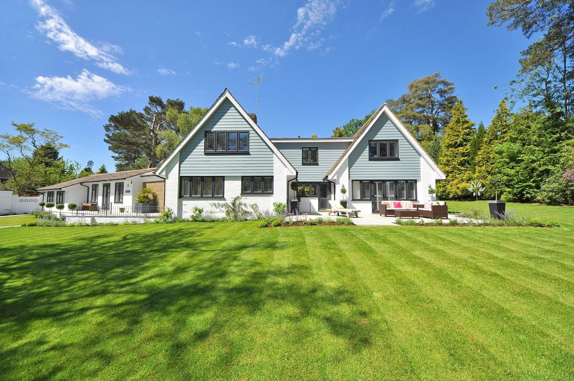 Two-story house with light blue siding, black window frames, and green lawn on a sunny day.